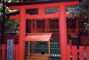 A photo of a Shinto shrine by a path in the woods at Nara in Japan,
 the red, wooden components of the temple dominating the image.